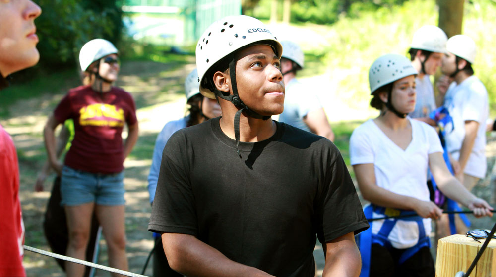 A group of people wearing safety helmets prepare for a rope course