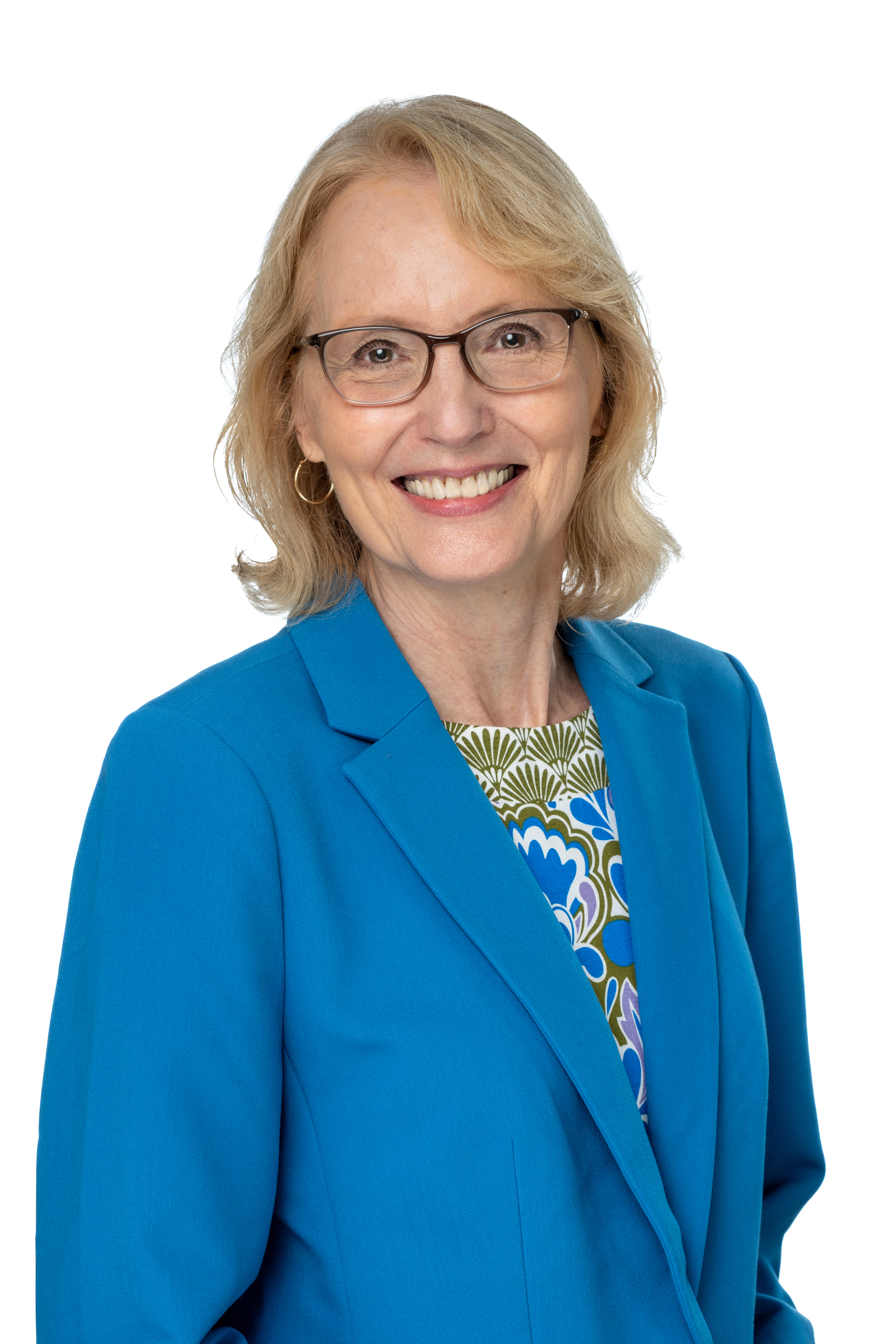 Katherine Tyson McCrea, PhD, smiling and wearing glasses, a bright blue blazer, and a patterned blouse with blue and green accents, against a light gray background.